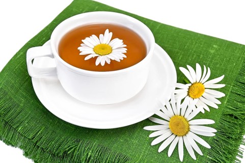 Herbal tea in a white cup with daisies on the green napkin, isolated on a white background