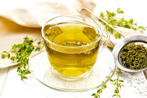 Herbal tea in a glass cup of thyme, a metal strainer with dry leaves, a linen napkin on the