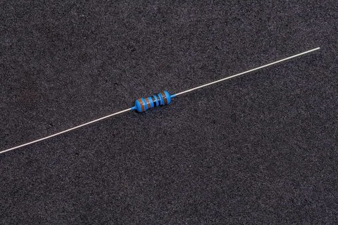 A blue-striped resistor with long leads on a dark background