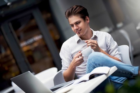 Handsome caucasian young man working on laptop and smiling while enjoying coffee in cafe