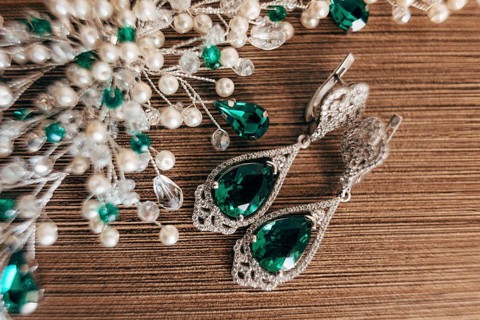 Earrings with a large emerald and an ornament of white beads on a brown background with a rough