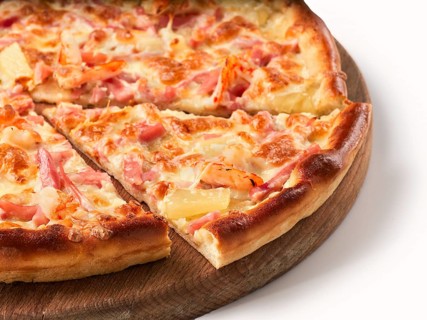 Close up view on piece of pizza with ham and pineapple on wooden cutting board. Isolated on white