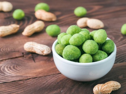 Peanut snack for beer, wine, party bar. Salted peanuts in green vasabi glaze on brown wooden table.