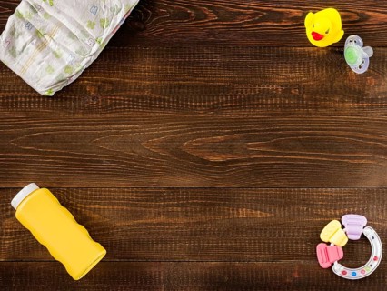 Disposable diaper, teether, dummy, baby powder and rubber duckling on dark wooden background with