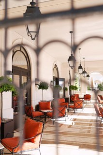 View through the wrought-iron lattice onto the hotel terrace with soft chairs and tables.