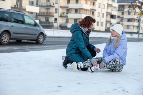 A woman who has fainted is sitting on the sidewalk. The sidewalk is covered with snow. Next to the