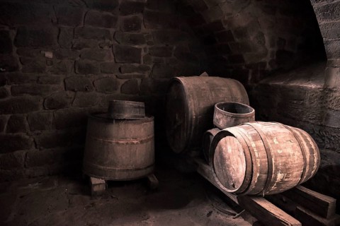 Vintage image with the interior of a stone wine cellar and aged wooden barrels, in low light.