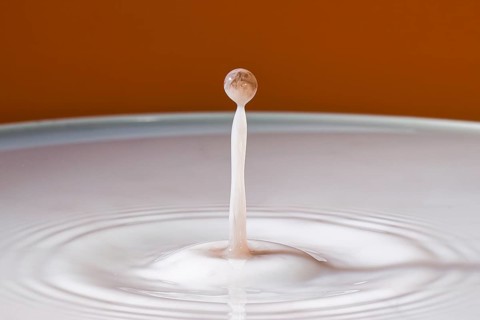 Single dripping water jet hits smooth surface in front of orange background, water droplets,