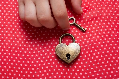 Hand holding a heart shaped lock and key on a red background