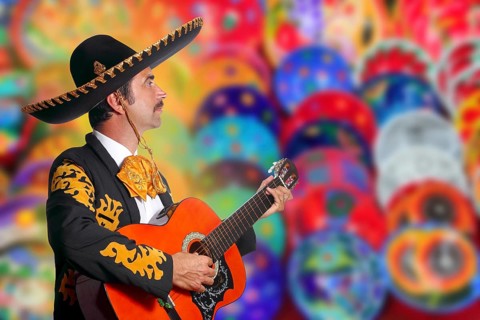 Charro Mariachi playing guitar over colorful blur handcrafts background