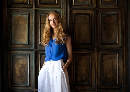 Portrait of the blonde woman in blue blouse staying in front of dark wall and keep smiling