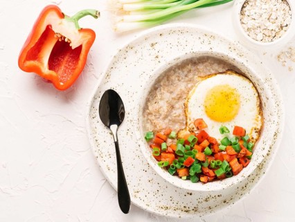 Savory oatmeal in craft trendy bowl, served with vegetables and fried egg on white concrete