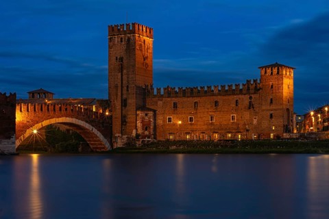 Majestic castle with bridge illuminated against the night sky with mirror-smooth river, at the blue