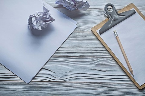 Crumpled paper balls and small clipboard with pencil on vintage white wooden boards