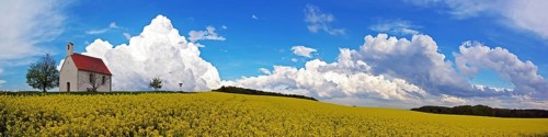 Panorama, chapel and storm clouds over a rapeseed field