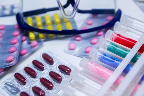 An arrangement of colorful pills and test tubes with safety glasses nearby