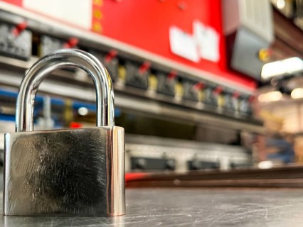 Image of a metal padlock in the foreground against the background of a metal bending machine.