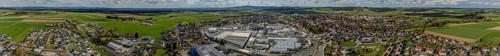 Expansive panorama of a town in a green landscape with fields and forests under a cloudy sky,