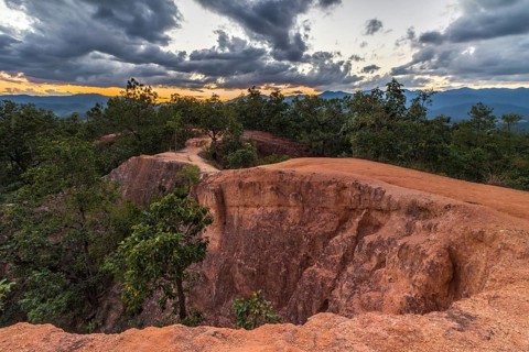Canyon near Pai city cloudy sky at sunset. Red sandy path and rocky walls. Mae Hong Son province,