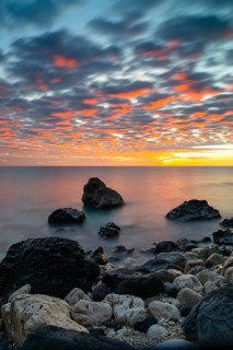 A colorful sunrise at Cala Gonone with black and white rocks and boulders in the foreground