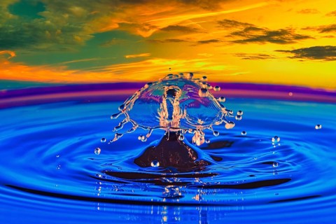 A drop of water in the middle of a lake with a colourful sunset in the background, highspeed