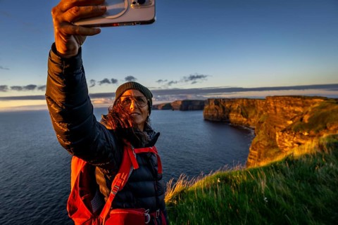 Female hiker taking a selfie, Cliffs of Moher, The Burren, County Clare, Ireland, United Kingdom,