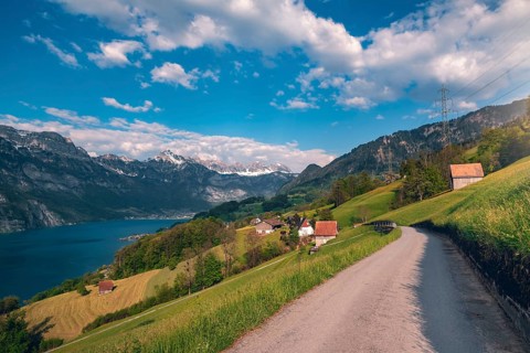 Spring landscape with country road toward a village, near Walensee lake and the Alps mountains,