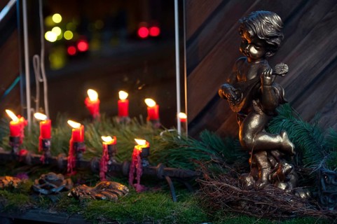 A golden angel figure next to a row of burning red candles on moss, borken, münsterland, germany