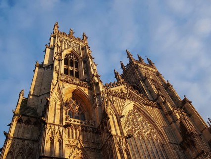A front view of the towers at the entrance to york minster in sunlight against a blue cloudy sky