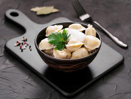 Traditional russian pelmeni, ravioli, dumplings with meat on black cutting board over black