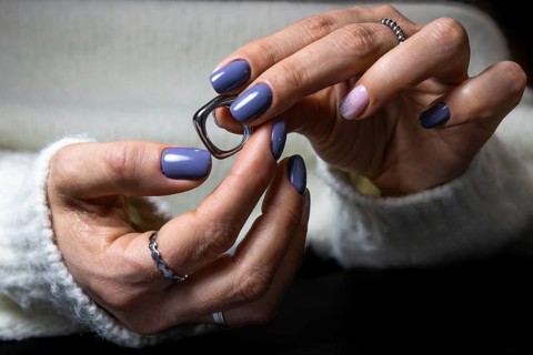 A woman's manicured hands with blue and pink nails hold a pair of eyeglasses, featuring elegant