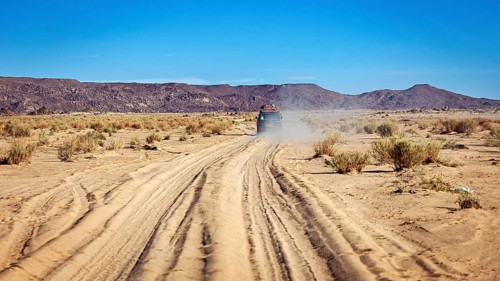 An off-road vehicle drives on a dusty sandy track in an arid desert, With the off-road vehicle