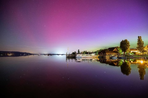 In a calm lake, the vivid northern lights are reflected next to boats and trees, harbour,