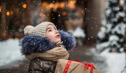 Happy girl with a gift box for Christmas catches snowflakes with his tongue on a city in winter
