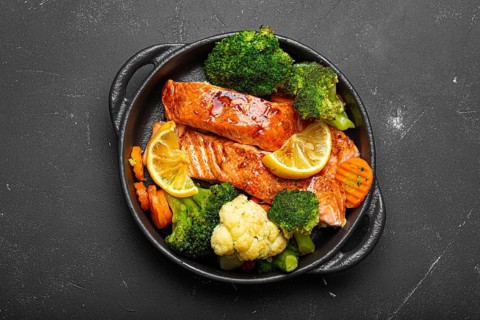 Healthy baked fish salmon steaks, broccoli, cauliflower, carrot in cast iron casserole bowl black