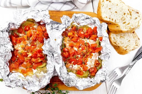 Pink salmon with zucchini, tomatoes, onions, garlic and thyme, baked in foil, fork and bread on the