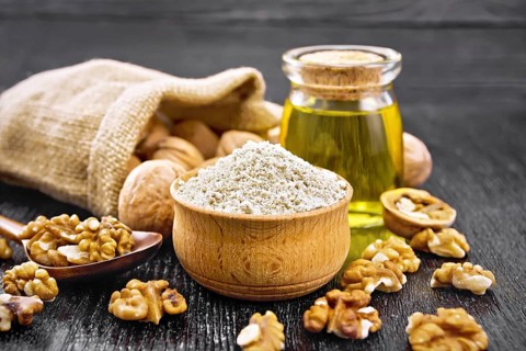 Walnut flour in bowl, nuts on a table, in a spoon and in a bag, oil in glass jar on wooden board