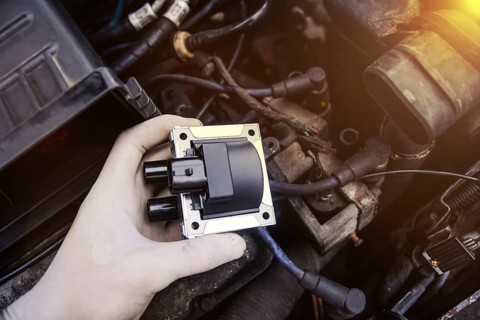 Hand holds car part with engine components around, highlighted by warm lighting