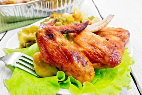 Fried chicken wings with vegetables and salad leaves on a plate, fork on the background light