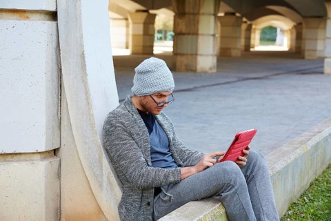 Modern young man with tablet pc touch working under a bridge with wool winter cap