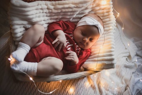 A cute newborn baby in xmas clothes sleeping in a basket on the floor against a Christmas