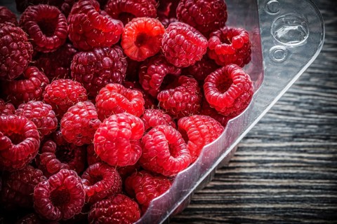 Red raspberry in container on wooden board