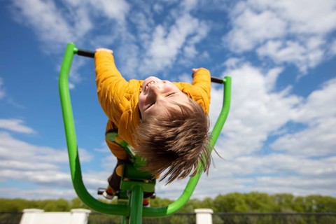 Funny little boy on a swing with his head down. Happy child on a walk. Ten year old boy against the