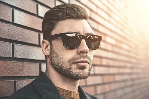 Portrait of stylish handsome young man with bristle standing outdoors and leaning on brick wall.