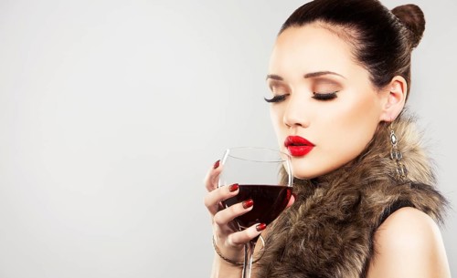 Beautiful woman with dark makeup and red lipstick posing on light grey background. Drinking glass