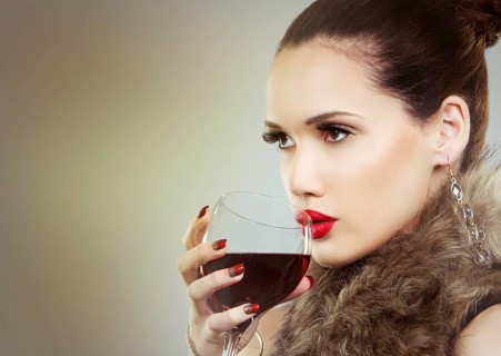 Beautiful woman with dark makeup and red lipstick posing on light grey background. Drinking glass