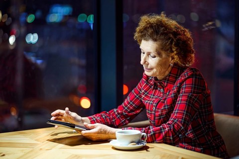 Mature woman with blond curly hair checks mail and social media notifications via tablet, smiling