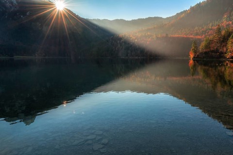 Contemplative autumn landscape with wooded hills, autumn forest, and the Alpsee lake, on a sunny