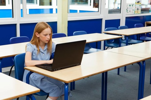 Primary school caucasian girl using a laptop in an empty classroom