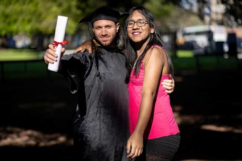 Young recently graduated man, dressed in cap and gown, with his degree in hand, celebrating with